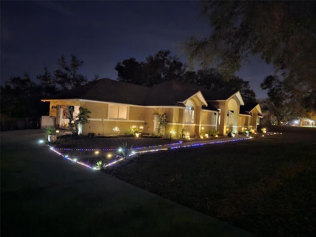 back of house at night featuring driveway and a fenced in pool