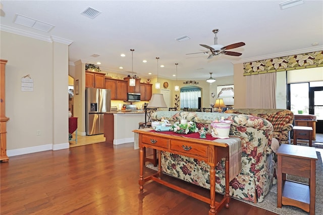 living room with crown molding, visible vents, a ceiling fan, and a wealth of natural light