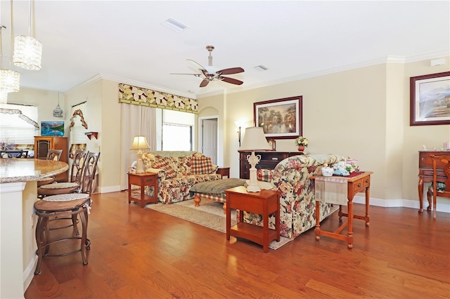 living room featuring wood finished floors, ceiling fan with notable chandelier, baseboards, ornamental molding, and visible vents
