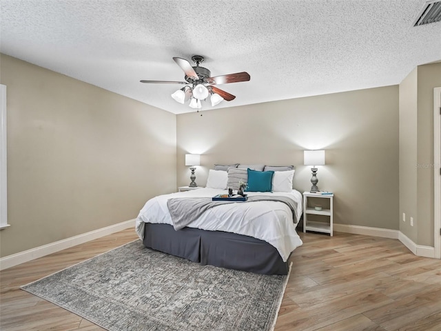 bedroom featuring a textured ceiling, visible vents, baseboards, and light wood-type flooring