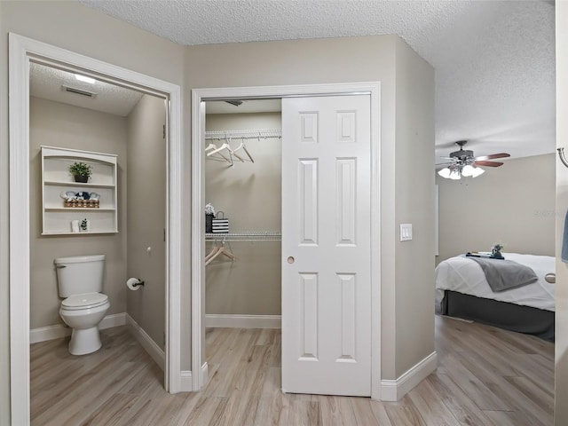 bathroom with a ceiling fan, a textured ceiling, visible vents, wood finished floors, and toilet
