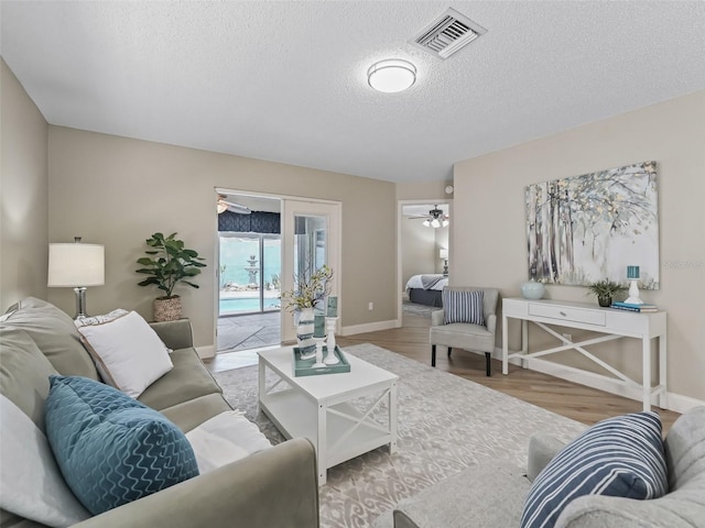 living area with ceiling fan, a textured ceiling, baseboards, wood finished floors, and visible vents