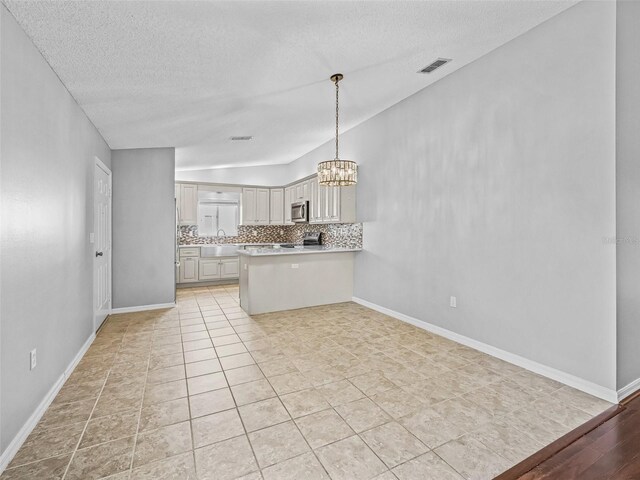 kitchen featuring stainless steel microwave, backsplash, light countertops, a peninsula, and a chandelier
