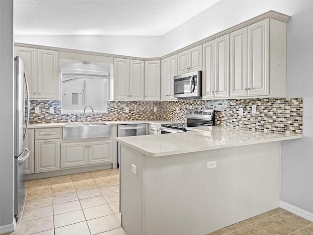kitchen with appliances with stainless steel finishes, a sink, a peninsula, light countertops, and light tile patterned floors