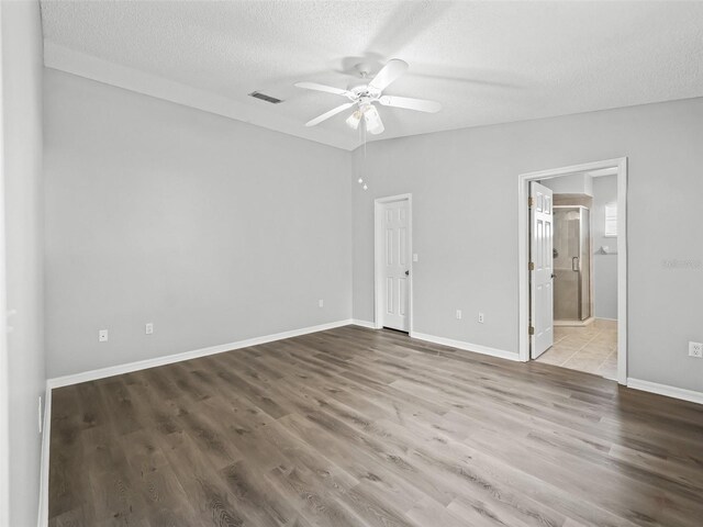 unfurnished bedroom featuring a textured ceiling, wood finished floors, ensuite bathroom, baseboards, and ceiling fan