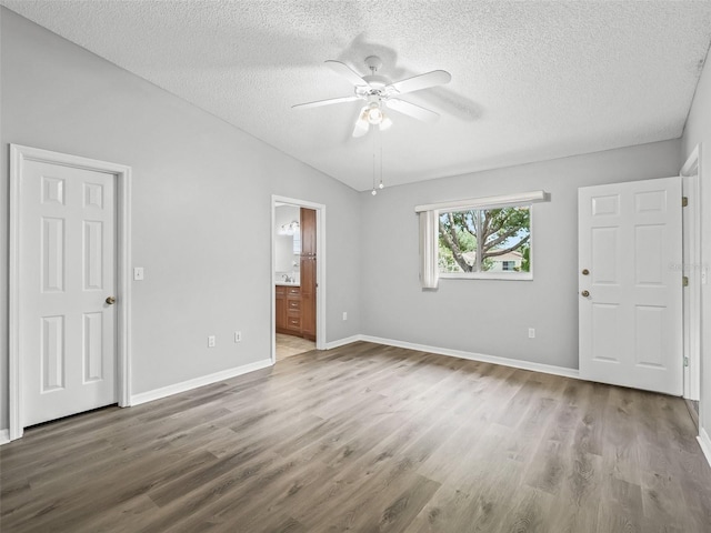 unfurnished bedroom featuring a textured ceiling, wood finished floors, baseboards, connected bathroom, and ceiling fan