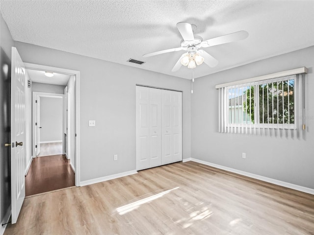 unfurnished bedroom featuring wood finished floors, a textured ceiling, a closet, baseboards, and a ceiling fan