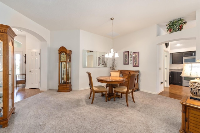 dining room with visible vents, light colored carpet, arched walkways, baseboards, and a notable chandelier