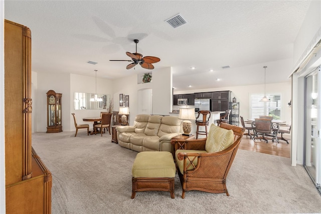living room featuring visible vents, baseboards, ceiling fan with notable chandelier, and light carpet
