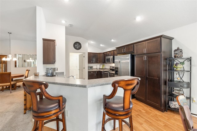 kitchen with a peninsula, dark brown cabinets, a kitchen breakfast bar, appliances with stainless steel finishes, and vaulted ceiling