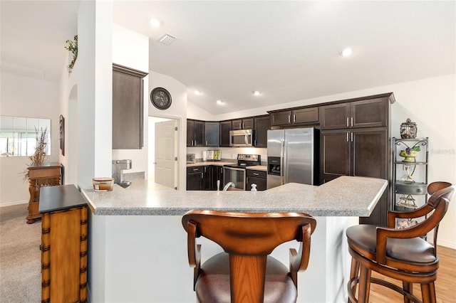 kitchen with a breakfast bar area, a peninsula, appliances with stainless steel finishes, and vaulted ceiling