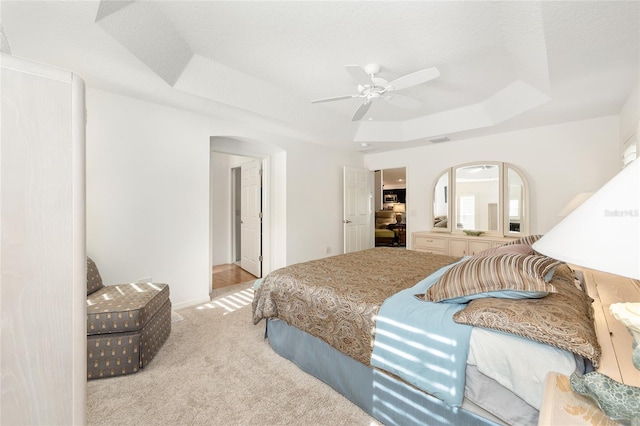 bedroom featuring a raised ceiling, a ceiling fan, arched walkways, and light colored carpet