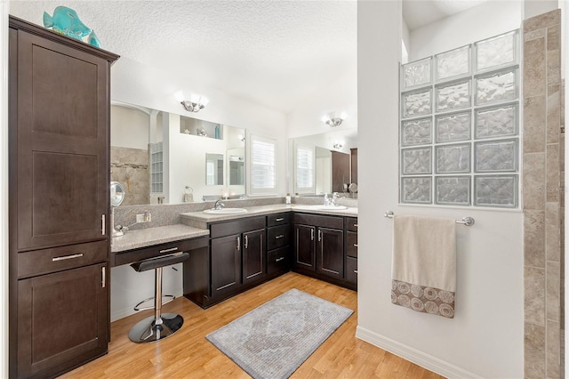 full bath featuring double vanity, a textured ceiling, a sink, and wood finished floors
