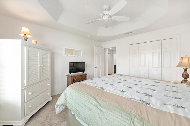 bedroom with ceiling fan, visible vents, a closet, light carpet, and a tray ceiling