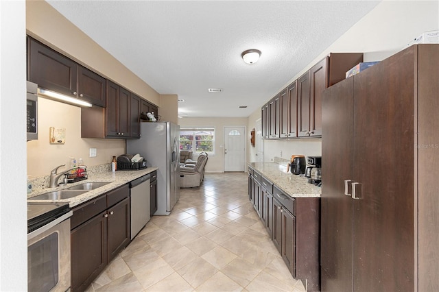 kitchen featuring dark brown cabinets, light tile patterned floors, a sink, light stone countertops, and appliances with stainless steel finishes