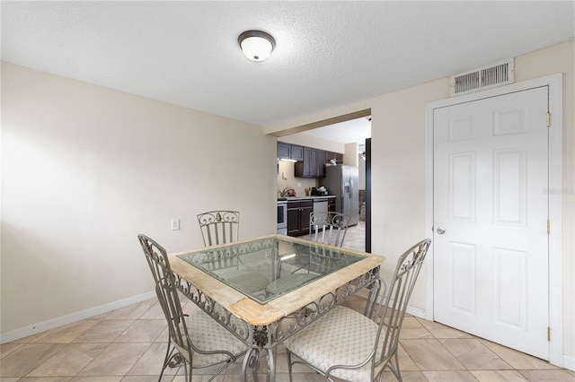 dining room featuring baseboards, visible vents, a textured ceiling, and light tile patterned floors