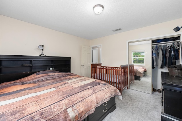 bedroom featuring light carpet, a textured ceiling, visible vents, and a closet