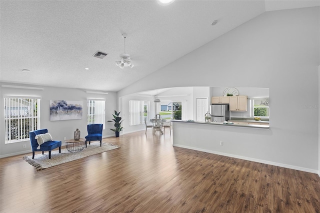 living room with wood finished floors, visible vents, plenty of natural light, and high vaulted ceiling