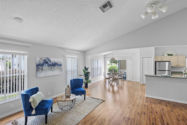 living area with a textured ceiling, ceiling fan, visible vents, baseboards, and light wood-type flooring