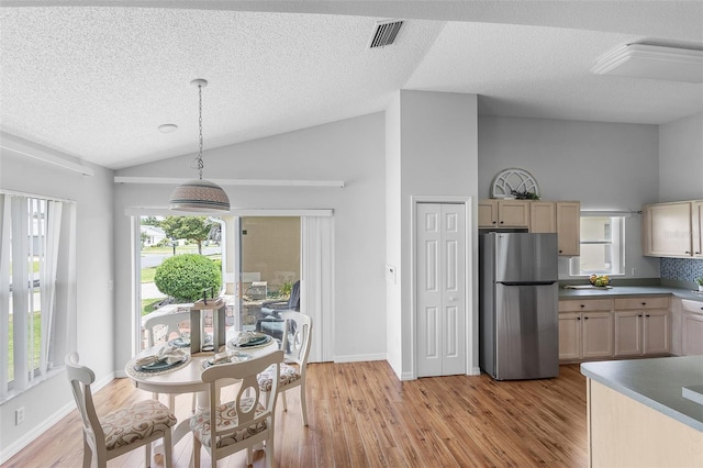 dining room with visible vents, a textured ceiling, light wood-style flooring, and vaulted ceiling
