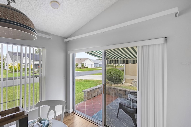 doorway with wood finished floors, a textured ceiling, and vaulted ceiling