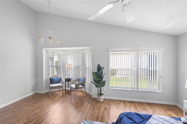 sitting room featuring wood finished floors, plenty of natural light, vaulted ceiling, and ceiling fan with notable chandelier