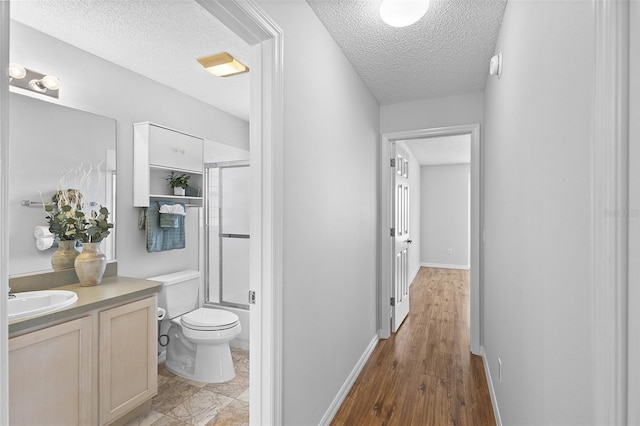 full bath featuring toilet, vanity, baseboards, bath / shower combo with glass door, and a textured ceiling