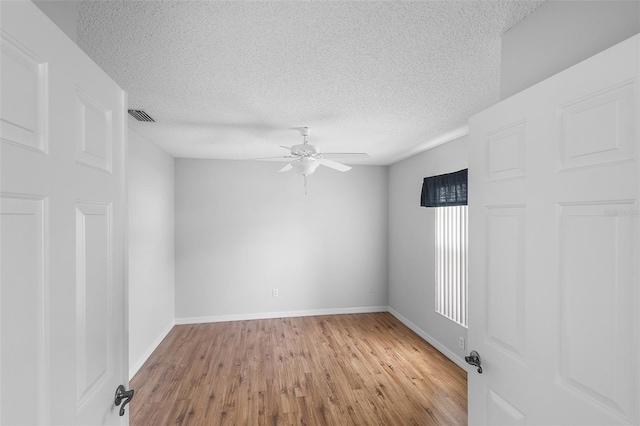 unfurnished room featuring wood finished floors, ceiling fan, baseboards, visible vents, and a textured ceiling