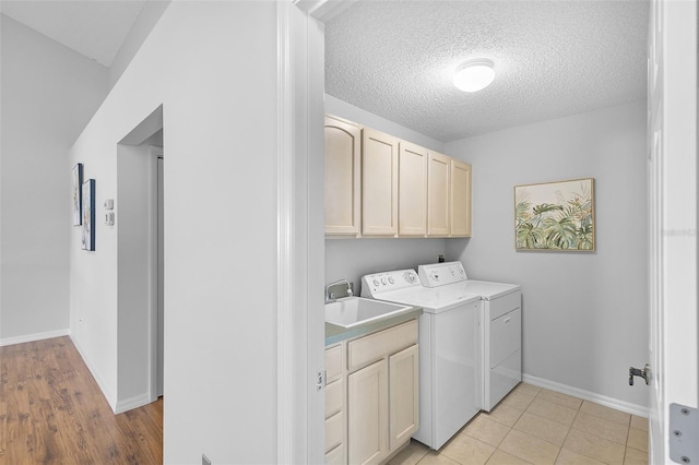 clothes washing area featuring a textured ceiling, a sink, baseboards, washer and dryer, and cabinet space