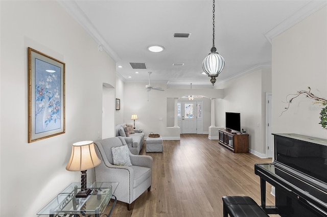 living room with ceiling fan, visible vents, ornamental molding, arched walkways, and wood finished floors