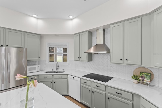 kitchen featuring light stone countertops, white appliances, a sink, gray cabinetry, and wall chimney exhaust hood