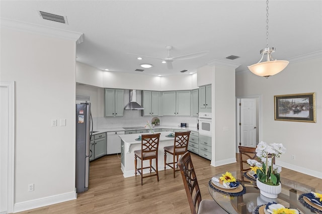 kitchen featuring white appliances, a breakfast bar area, light countertops, wall chimney range hood, and ornamental molding