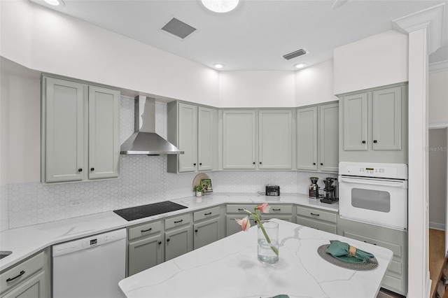 kitchen with visible vents, gray cabinetry, wall chimney exhaust hood, white appliances, and backsplash