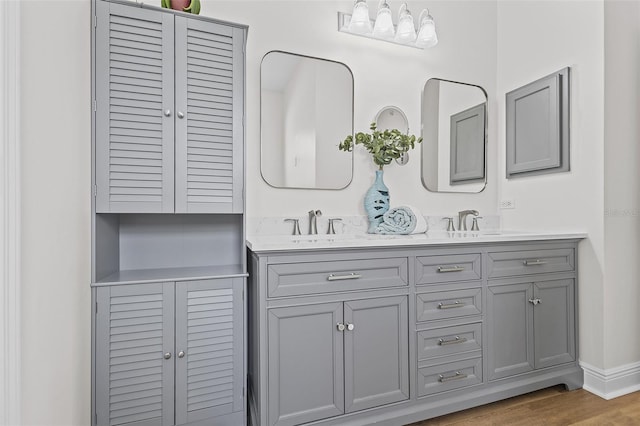 bathroom with baseboards, wood finished floors, double vanity, and a sink