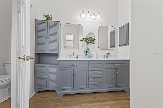 bathroom featuring double vanity, wood finished floors, toilet, and a sink