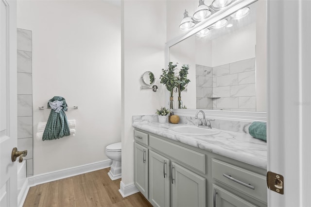 bathroom featuring wood finished floors, walk in shower, toilet, vanity, and baseboards