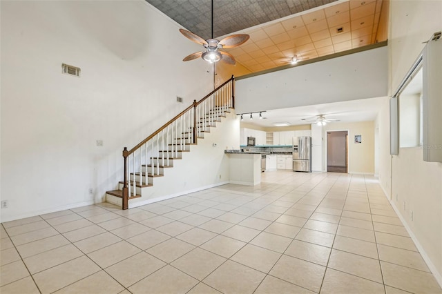 unfurnished living room featuring light tile patterned flooring, ceiling fan, visible vents, and a towering ceiling