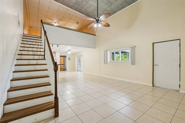 interior space with ceiling fan, baseboards, light tile patterned floors, a towering ceiling, and stairway
