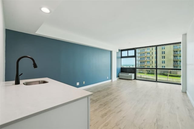 kitchen with baseboards, light wood-type flooring, light countertops, expansive windows, and a sink