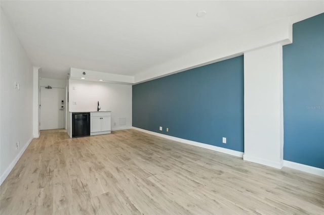 unfurnished living room with baseboards, a sink, light wood-style flooring, and bar