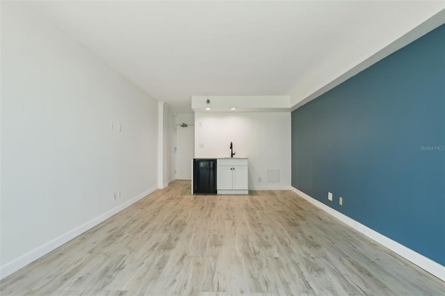 unfurnished living room featuring baseboards, a sink, light wood-style flooring, and recessed lighting