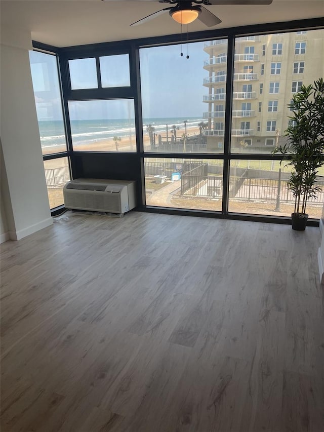 spare room with baseboards, a ceiling fan, wood finished floors, and a wall of windows
