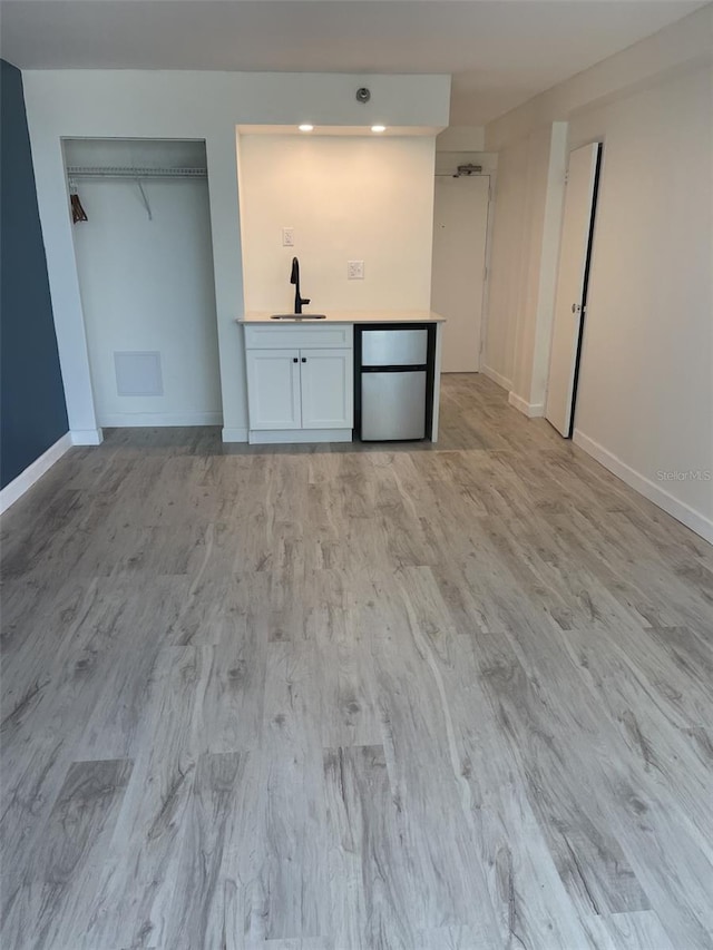 unfurnished bedroom with baseboards, a sink, light wood-style flooring, and fridge