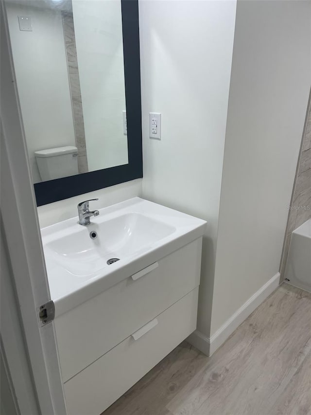full bath featuring a tub, baseboards, wood finished floors, and vanity