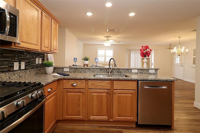 kitchen featuring appliances with stainless steel finishes, a sink, ceiling fan with notable chandelier, stone counters, and backsplash