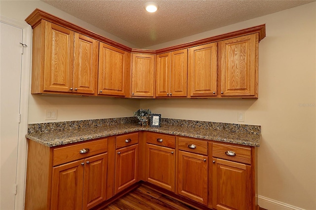 kitchen with brown cabinets, dark wood-style floors, and dark stone countertops