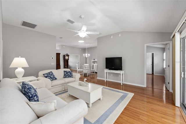 living area with ceiling fan with notable chandelier, visible vents, light wood-type flooring, and vaulted ceiling