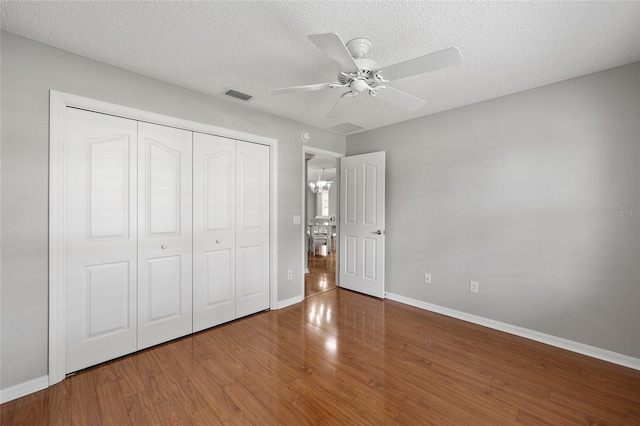 unfurnished bedroom featuring wood finished floors, a closet, baseboards, visible vents, and a textured ceiling