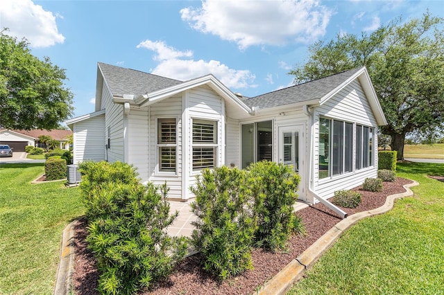 view of property exterior with a yard, a shingled roof, central AC unit, and a sunroom