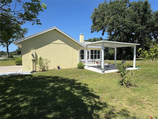 back of house with stucco siding, a chimney, a yard, and a patio
